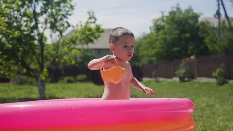 Little boy stands in inflatable pool and pours water out of toy watering can Video stock 197061146