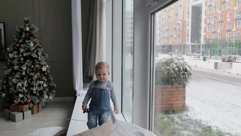 A little boy stands by the window in the winter during the Christmas holidays Stock Footage 166041158
