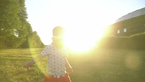A little boy in a star-patterned shirt runs joyfully across a green lawn, lookin Stock Footage 327852084