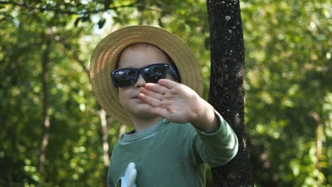 Little boy in a straw hat and sunglasses walking and playing in the garden Stock Footage 280339828
