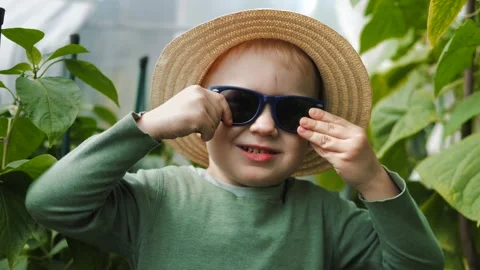 Little boy in a straw hat and sunglasses walking and playing in the garden Stock Footage 280339937