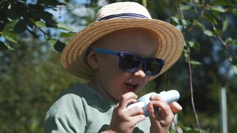 Little boy in a straw hat and sunglasses walking and playing in the garden Stock Footage 280339956