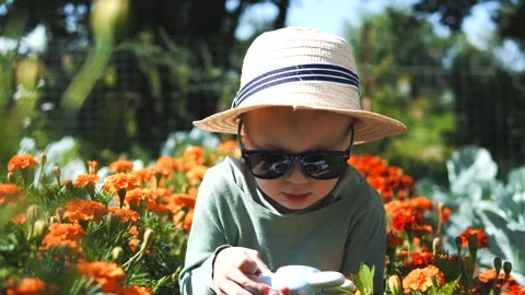 Little boy in a straw hat and sunglasses walking and playing in the garden Stock Footage 280340043