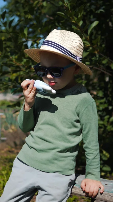 Little boy in a straw hat and sunglasses walking and playing in the garden Stock Footage 280340164