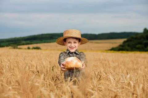 Little boy in the straw hat and shirt he held out his handing with bread in.. Stock Photos