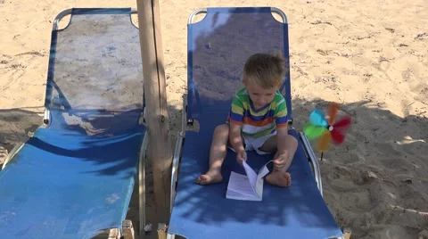 Little boy study book on sunbed near a pinwheel on the beach Stock Footage 62823967