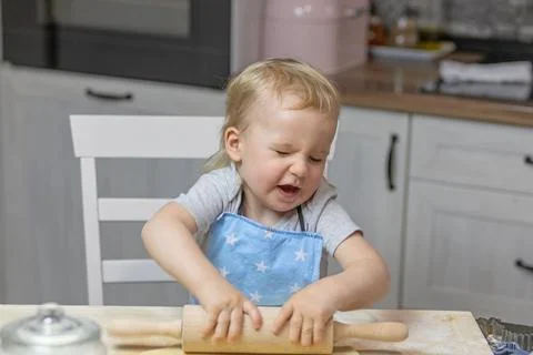 Little boy "suffers" while working with a wooden kitchen roller Stock Photos