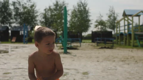 A little boy in swim trunks throws sand on the beach by the lake. The child Stock Footage 248049557