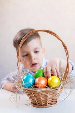 Little boy takes an Easter egg from the basket from the table on a white back 스톡 사진
