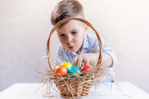 Little boy takes an Easter egg from a basket from the table on a white backgr 스톡 사진