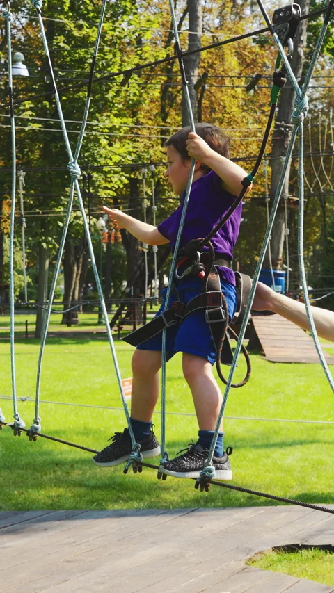 Little boy taking wide step on tightrope bridge in adventure park Stock Footage 345894538