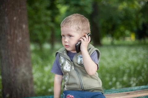 Little boy talking on the phone while sitting outdoors Stock Photos
