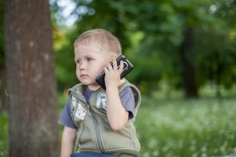 Little boy talking on the phone while sitting outdoors Stock Photos