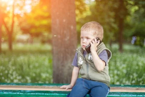 Little boy talking on the phone while sitting outdoors Stock Photos