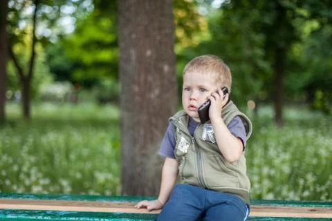 Little boy talking on the phone while sitting outdoors Stock Photos