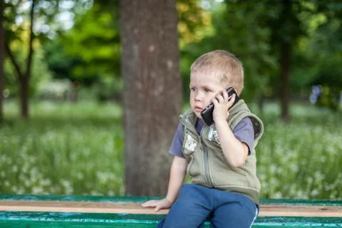Little boy talking on the phone while sitting outdoors Stock Photos