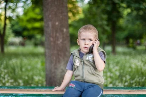 Little boy talking on the phone while sitting outdoors Stock Photos