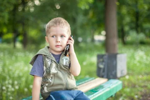 Little boy talking on the phone while sitting outdoors Stock Photos