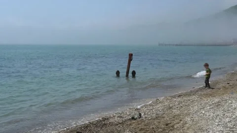 Little boy throws stones into sea. There is anchor not far from coast in sea. Stock Footage 154460853