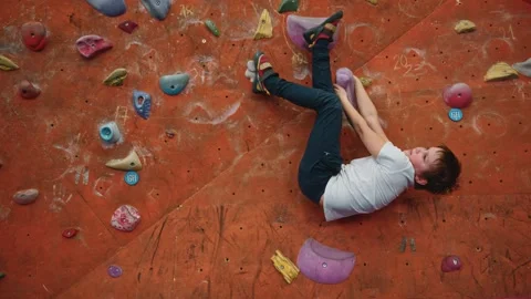 A little boy is training on a climbing wall indoors and turns upside down Stock Footage 276334264