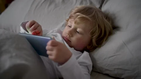 Little boy of two years old lies in cute bed and plays games on mobile phone Stock Footage 167232572