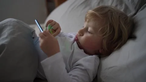 Little boy of two years old lies in cute bed and plays games on mobile phone Stock Footage 167232638