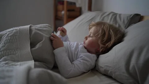 Little boy of two years old lies in cute bed and plays games on mobile phone Stock Footage 167232839