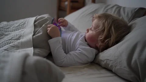 Little boy of two years old lies in cute bed  and plays games on mobile phone Stock Footage 167232900