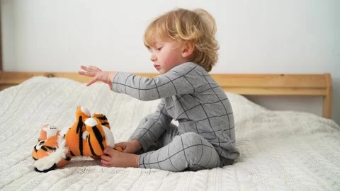 Little boy of two years old plays with toy tiger on the bed in cozy room Stock Footage 168067499