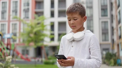 Little Boy is Typing Something on the Smartphone Standing Outside. Stock Footage 249823788