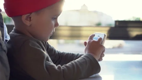 Little boy use app on smartphone in cafe sitting on the arms of his mother Stock Footage 78480107