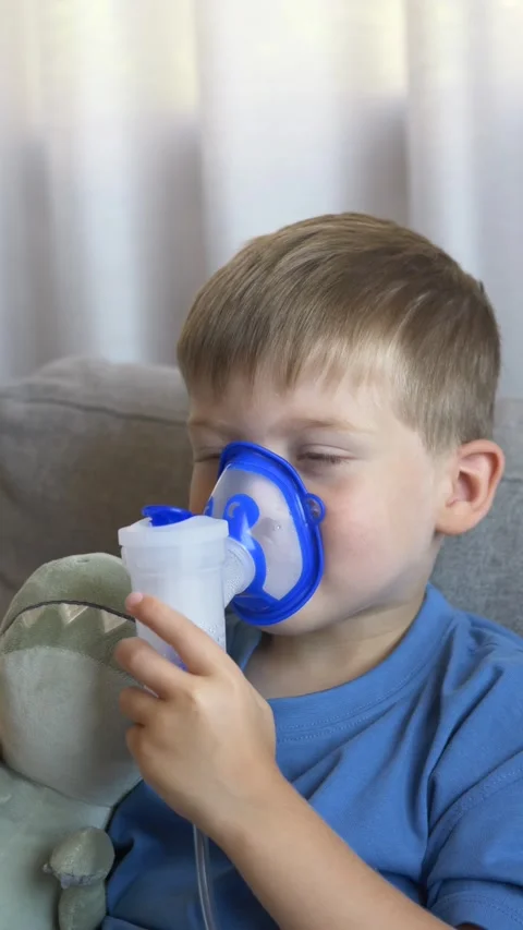 Little boy using a nebulizer while holding a plush toy during home inhalation Stock Footage 345654223