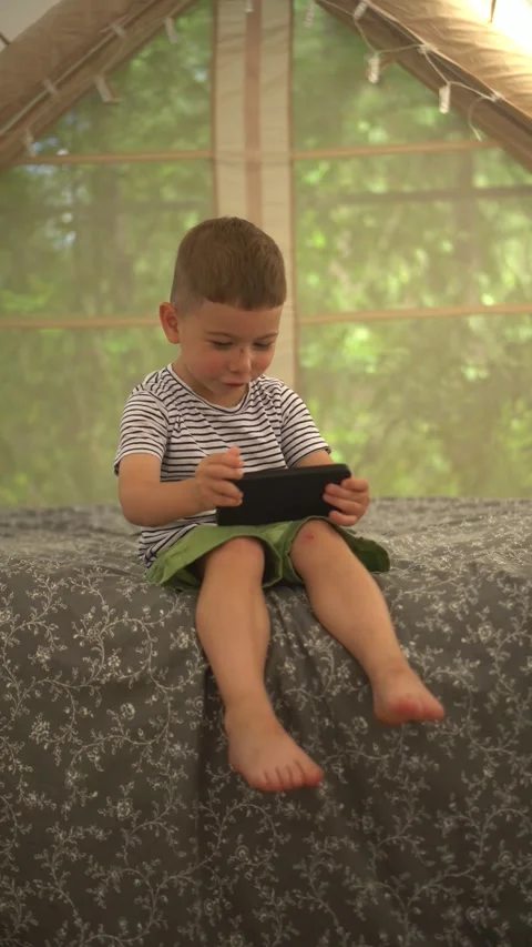Little Boy Using a Smartphone While Sitting Inside an Inflatable Tent Vídeos de archivo 343894555