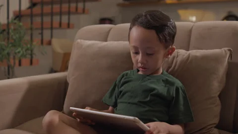Little boy using a tablet while sitting on a living room sofa Stock Footage 339868123