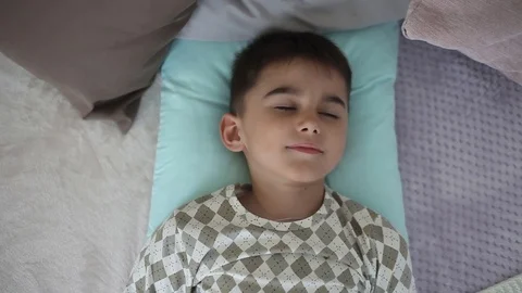 Little boy wakes up lying on a bed with pillows Stock Footage 90550376