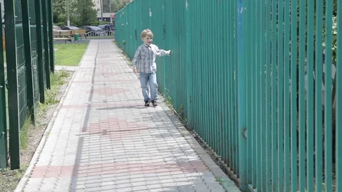 Little boy walks along the iron fence Stock Footage