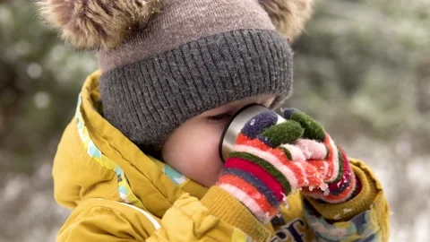 A little boy in a warm hat drinks hot tea from a cup outdoors in winter, steam Stock-Footage 144487699
