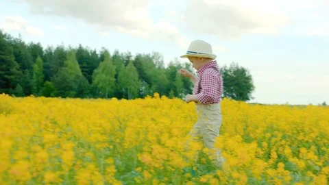Little boy wearing straw hat and trousers on suspenders ia walking at flowering Stock Footage 78892749