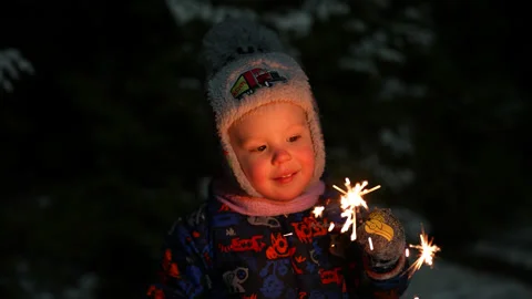 A little boy in a winter hat and blue overalls on Christmas night holds a Stock Footage 211503738