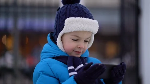 Little boy in winter wear using phone on cold snowy day Stock Footage 122609853