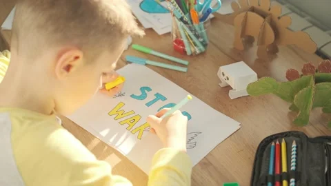 A little boy writes on paper a message to stop the war. No war, stop war Stock Footage 178897582