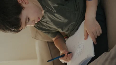Little boy writing in notebook on a sofa at home. Childhood learning development Stock Footage 260915454