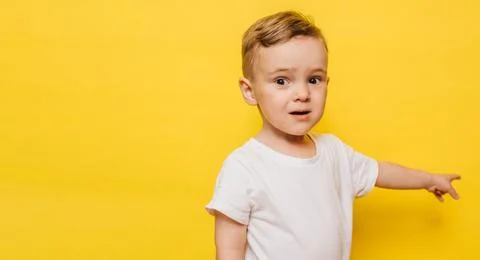 A little boy on a yellow background points to the background. Copy space. Stock Photos