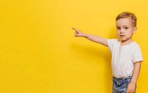 A little boy on a yellow background points to the background. Copy space. Stock Photos