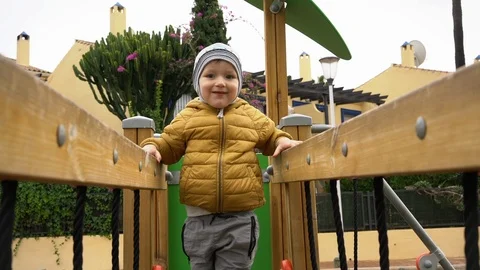 Little boy in a yellow jacket playing on a playground, tilt down Stock Footage 89773769