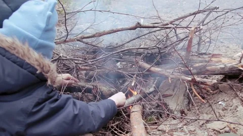 Little boys put branches in small campfire Stock Footage 76560544