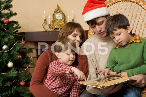 Little brothers pointing at page of book while their father reading it to them Stock Photos