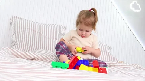 Little builder creating colorful structures with blocks on a cozy bed Vídeos de archivo 295350984