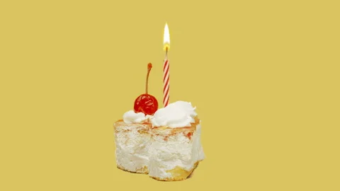  Little cake with cherry and burning candle, rotates on a yellow background. The Vídeos de archivo 120111744