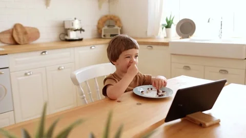 A little caucasian boy eats krunchy and watches tablet PC at kitchen table. Stock Footage 171775238
